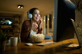 Young woman having fun while eating popcorn and watching movie